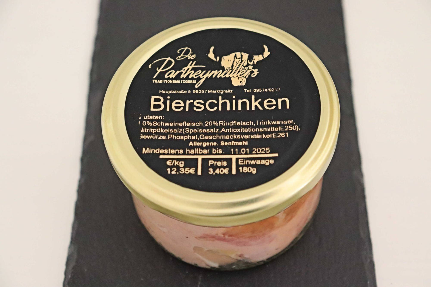 Ein Glas mit Bierschinken von der Firma Partheymüller, mit schwarzem Etikett auf goldenem Deckel.