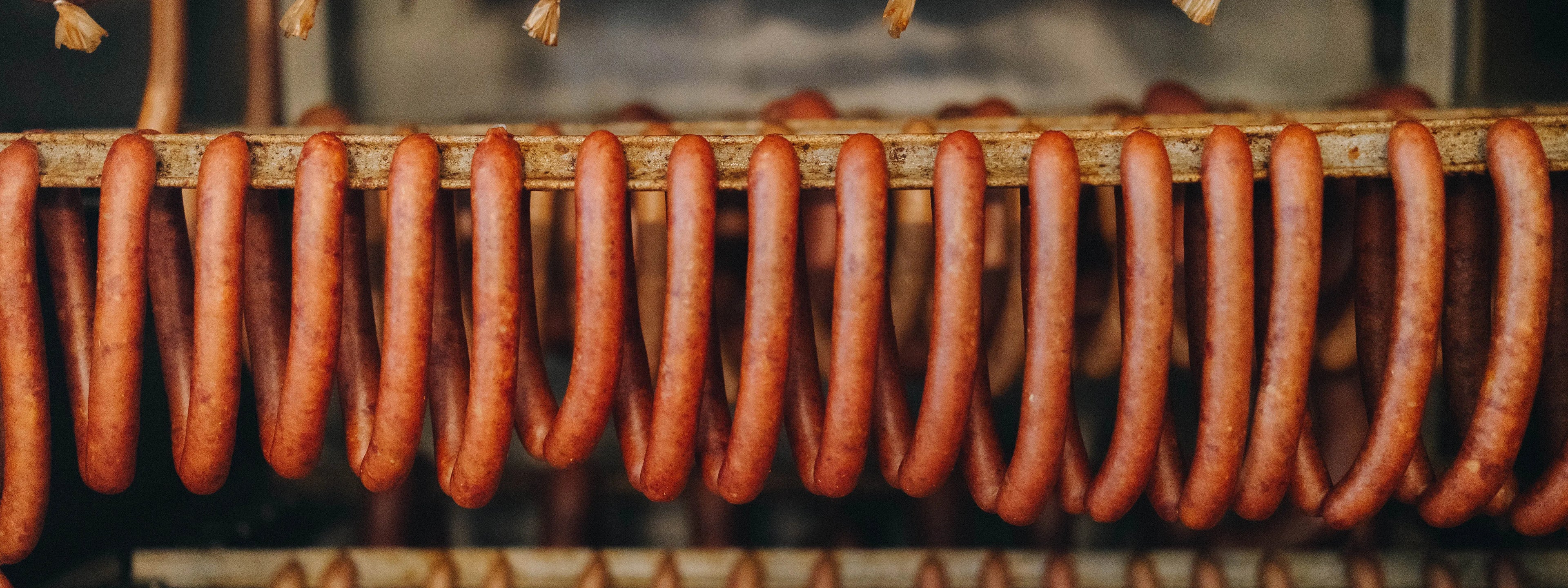 Eine Reihe geräucherter Bratwurst über einem Metallstab hängend.
