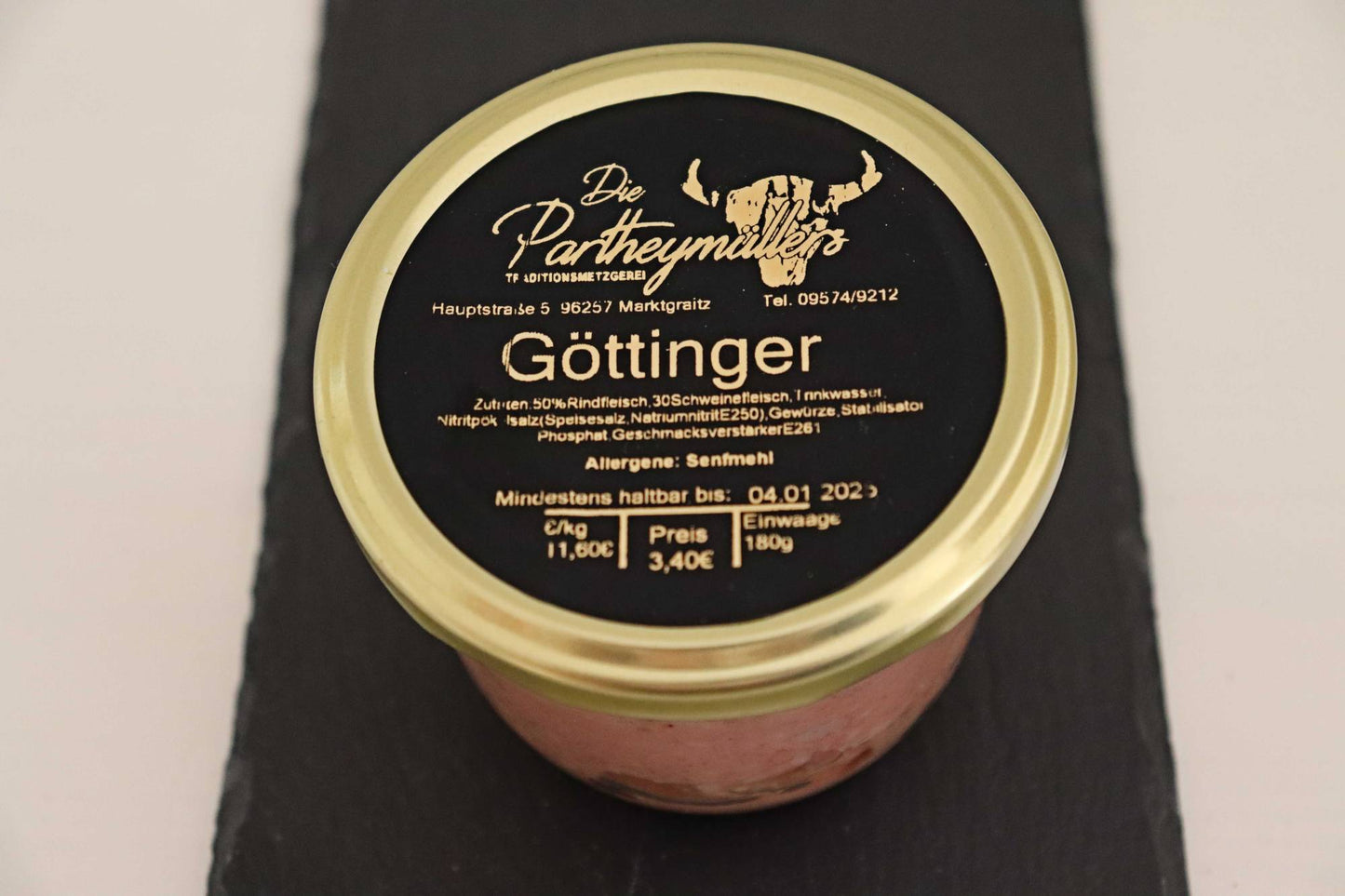 Ein Glas Goettinger Wurst mit goldenem Deckel und schwarzem Etikett von der Marke Partheymüller auf dunklem Untergrund.