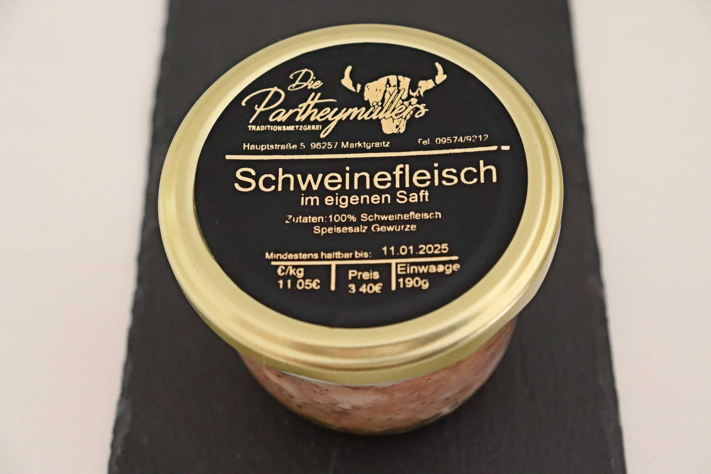 Ein Glas mit Schweinefleisch von der Firma Partheymüller, mit schwarzem Etikett auf goldenem Deckel.