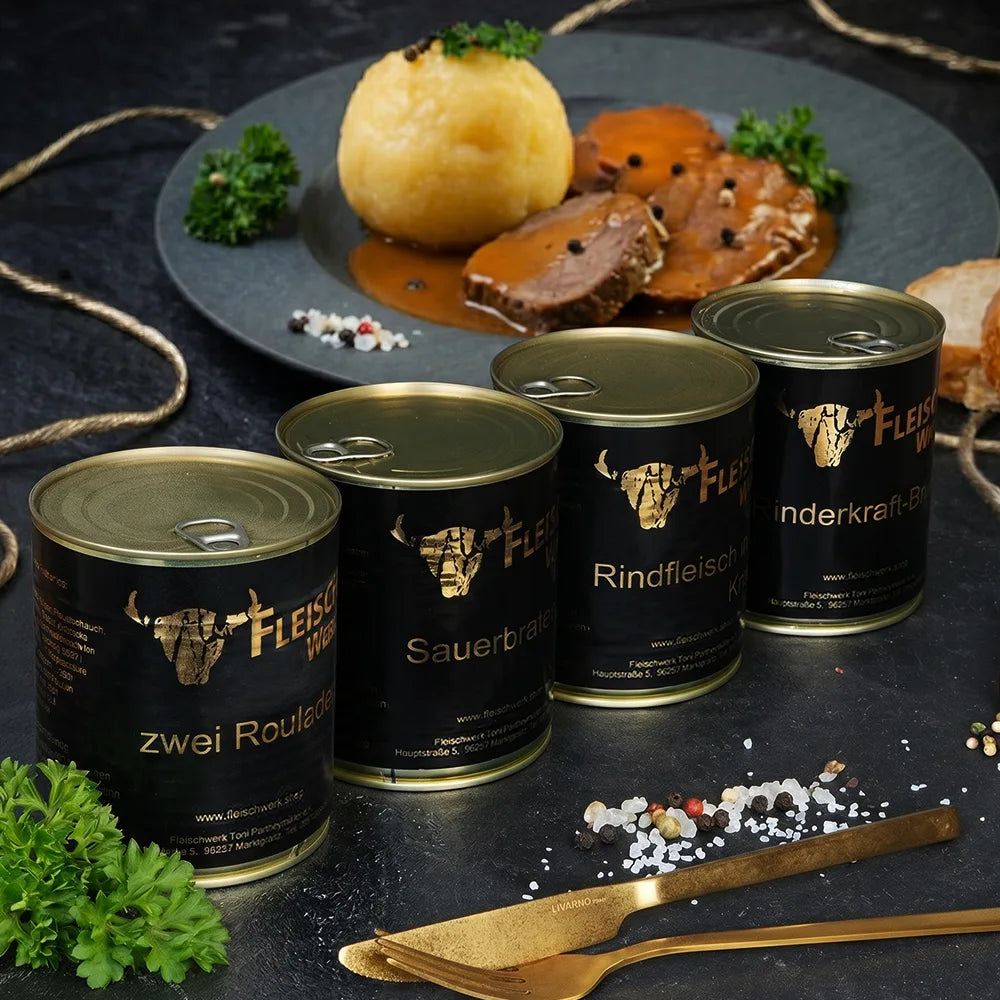 Vier Dosen mit dunklem Etikett  stehen auf dunkler Schieferplatte vor Teller mit Sauerbraten und Kloß.