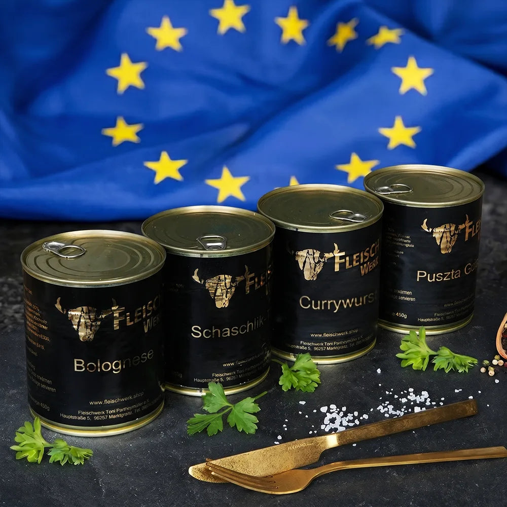 Vier Dosen mit dunklem Etikett stehen nebeneinander auf dunkler Schieferplatte vor einer Europa Flagge.