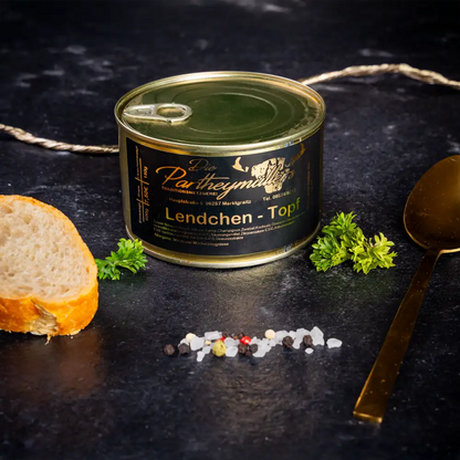 Kleine goldene Konservendose der Metzgerei Partheymüller mit Lendchentopf, edel präsentiert auf dunklem Untergrund mit frischen Kräutern, Pfefferkörnern, Meersalz und einer Baguettescheibe.