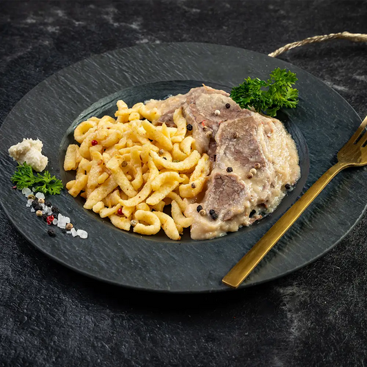 Rindfleisch in Meerrettichsauce mit Spätzle auf schwarzem Teller, garniert mit Petersilie, Pfefferkörnern und grobem Salz, links ein Klecks Meerrettich, rechts eine goldene Gabel, auf dunklem Untergrund